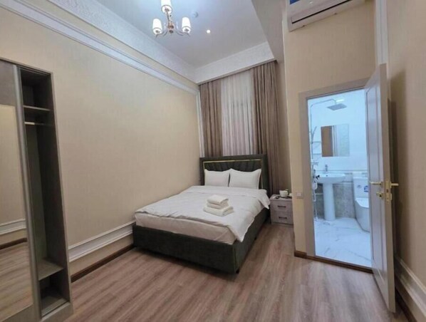 Une chambre à coucher avec un lit, des tables de chevet, une armoire et une salle de bain visible à travers une porte ouverte.