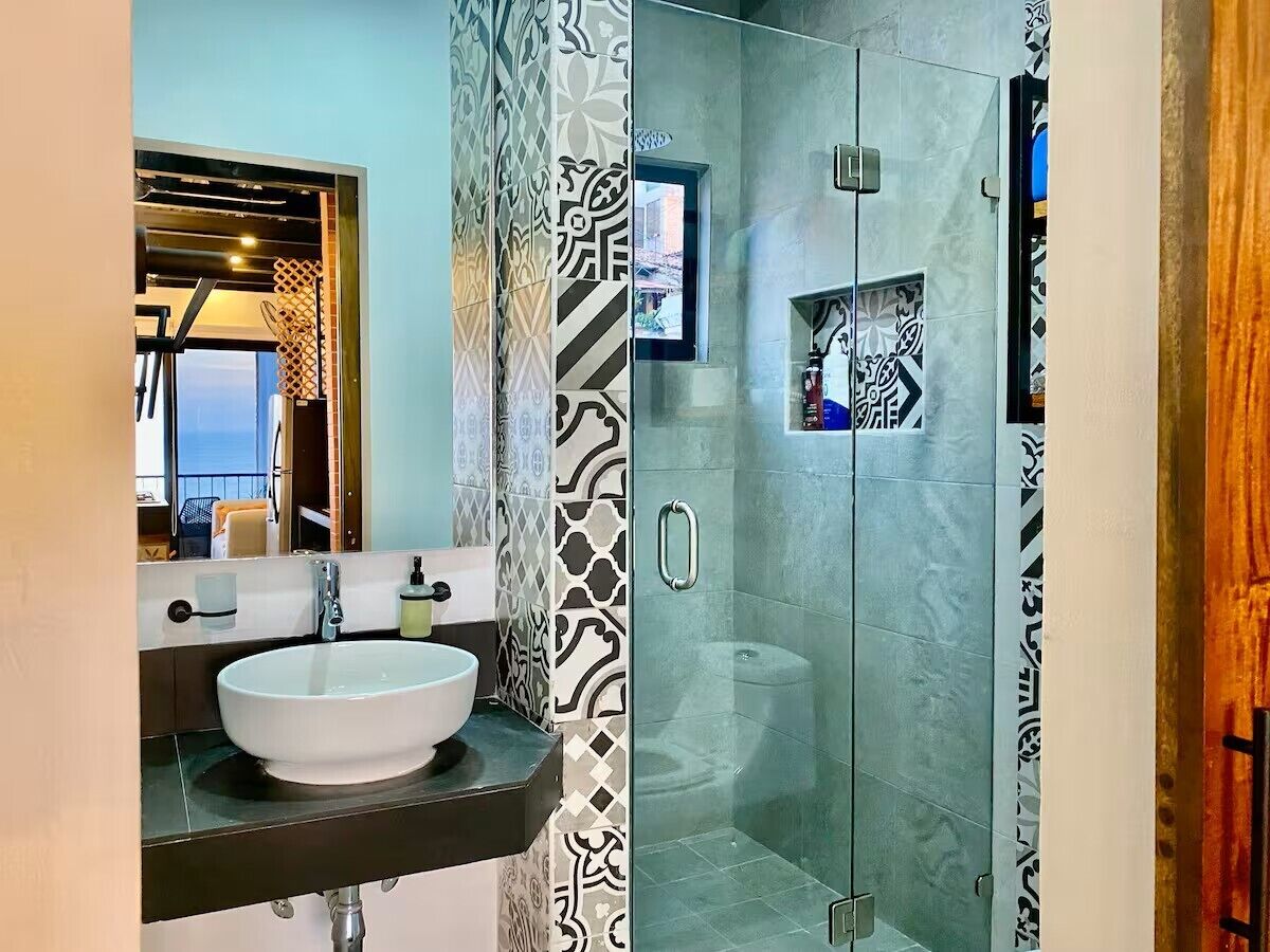 Un baño moderno con un lavamanos grande de color blanco, una cabina de ducha con mampara de vidrio y baldosas con diseño.