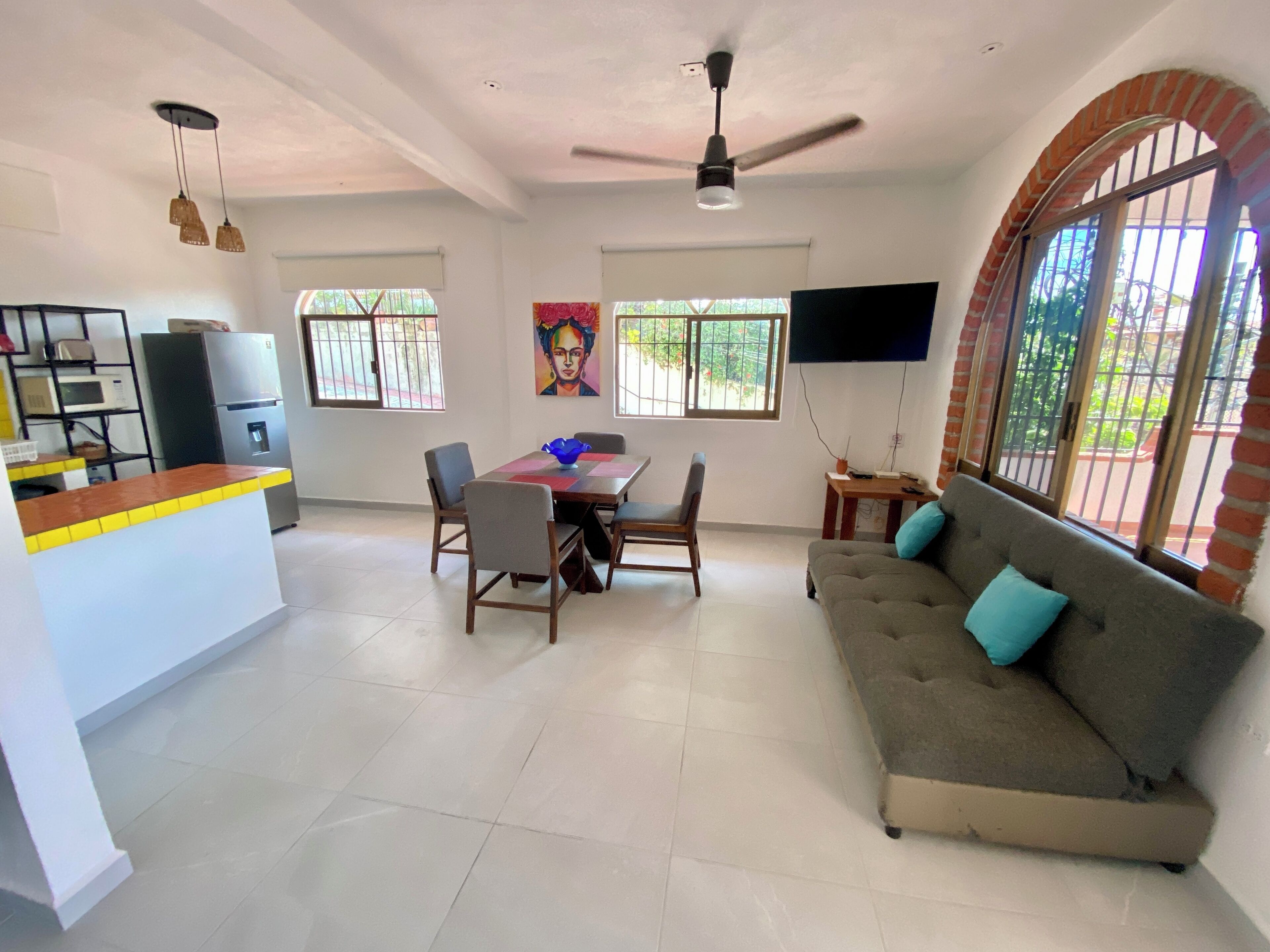 A spacious living area with a dining table, sofa, ceiling fan, TV, and kitchen appliances.