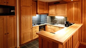 A kitchen with wooden cabinets, a black stove, a sink, and a coffee maker. - Parking, tv, ski locker, 71m², Les 2 Alpes (Les Deux Alpes)