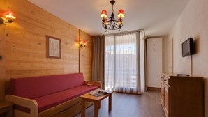 Ett mysigt rum med en väggpanel av trä, en röd soffa, ett träbord med ett tidningsnummer, en tv på väggen och ett fönster med gardiner.