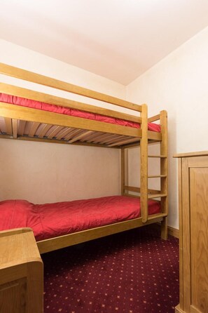 A bunk bed with a red mattress in a room with a patterned carpet.