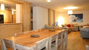 Ein Holzespeisesaal mit Stühlen, ein Küchenbereich mit Holzschränken und ein Wohnzimmer mit einer Couch und einem Gemälde an der Wand.