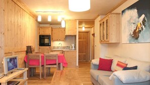 Ein gemütliches Wohnzimmer mit einer Couch und einem Esstisch, Holzwänden und einer Küche im Hintergrund.