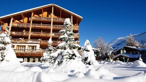 Ein mehrstöckiges Holzgebäude mit Balkonen, umgeben von schneebedeckten Bäumen und einem Berg im Hintergrund.