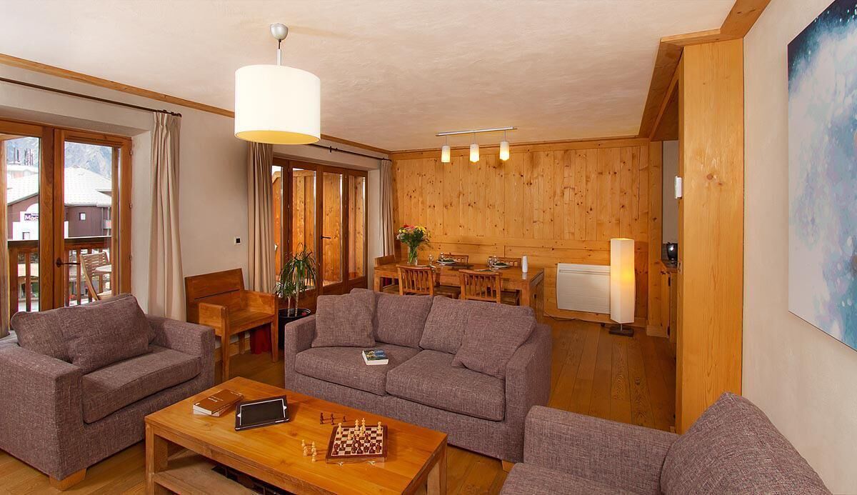Een gezellige woonkamer met een bank, een bijzettafeltje met een schaakbord, en een eethoek met een tafel en stoelen.