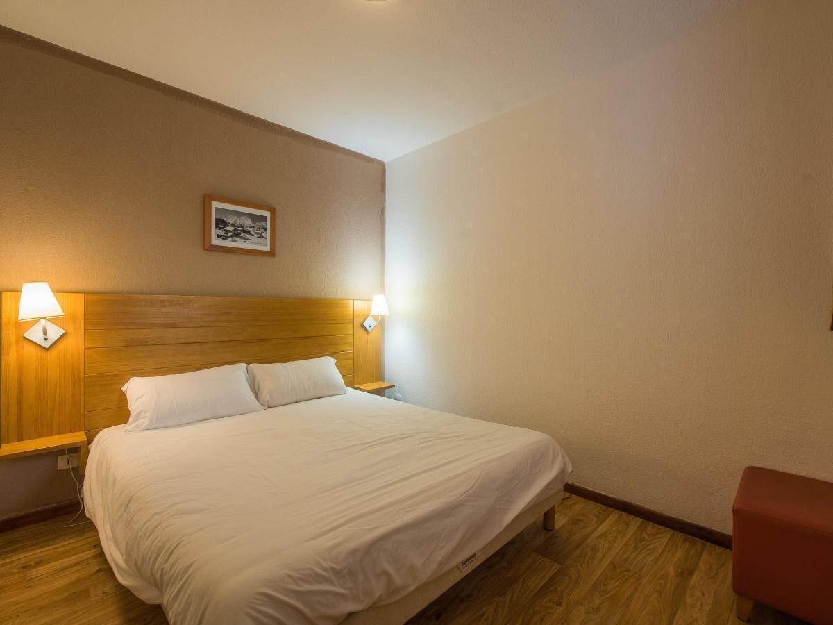 Een hotelkamer met een bed, een houten hoofdbord, twee wandlampen en een klein fotolijstje aan de muur.