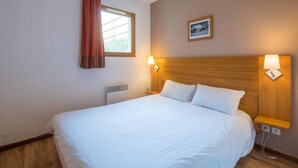 A hotel room with a large bed, two bedside lamps, a window with curtains, a radiator, and a framed picture on the wall.