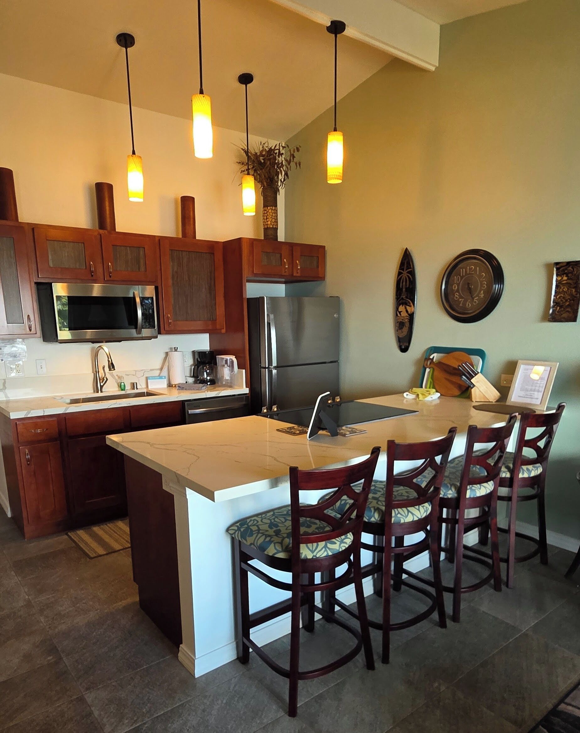 Una cocina moderna con una isla central, armarios de madera, un refrigerador de acero inoxidable e iluminación colgante.