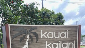 Une enseigne en bois avec le texte « Kauai Kailani » et une illustration représentant un palmier.