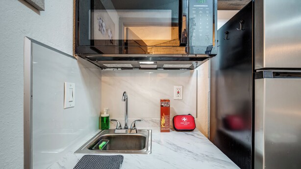 A compact kitchen with a stainless steel refrigerator, a microwave, and a sink. - Cozy Studio Just 5 Minutes from Miami Airport! Comes with 1 Free Parking Space. (Miami Springs)