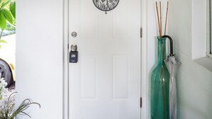 A white door with a "Welcome" sign, a doormat with "Be our guest" text, and a green vase with sticks. - Cozy Studio Just 5 Minutes from Miami Airport! Comes with 1 Free Parking Space. (Miami Springs)