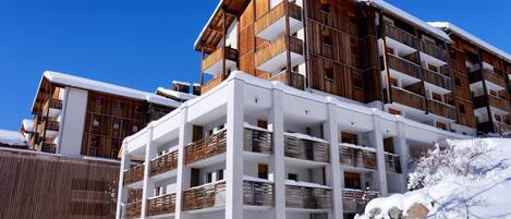 A multi-story hotel with wooden balconies and white walls, surrounded by snow.