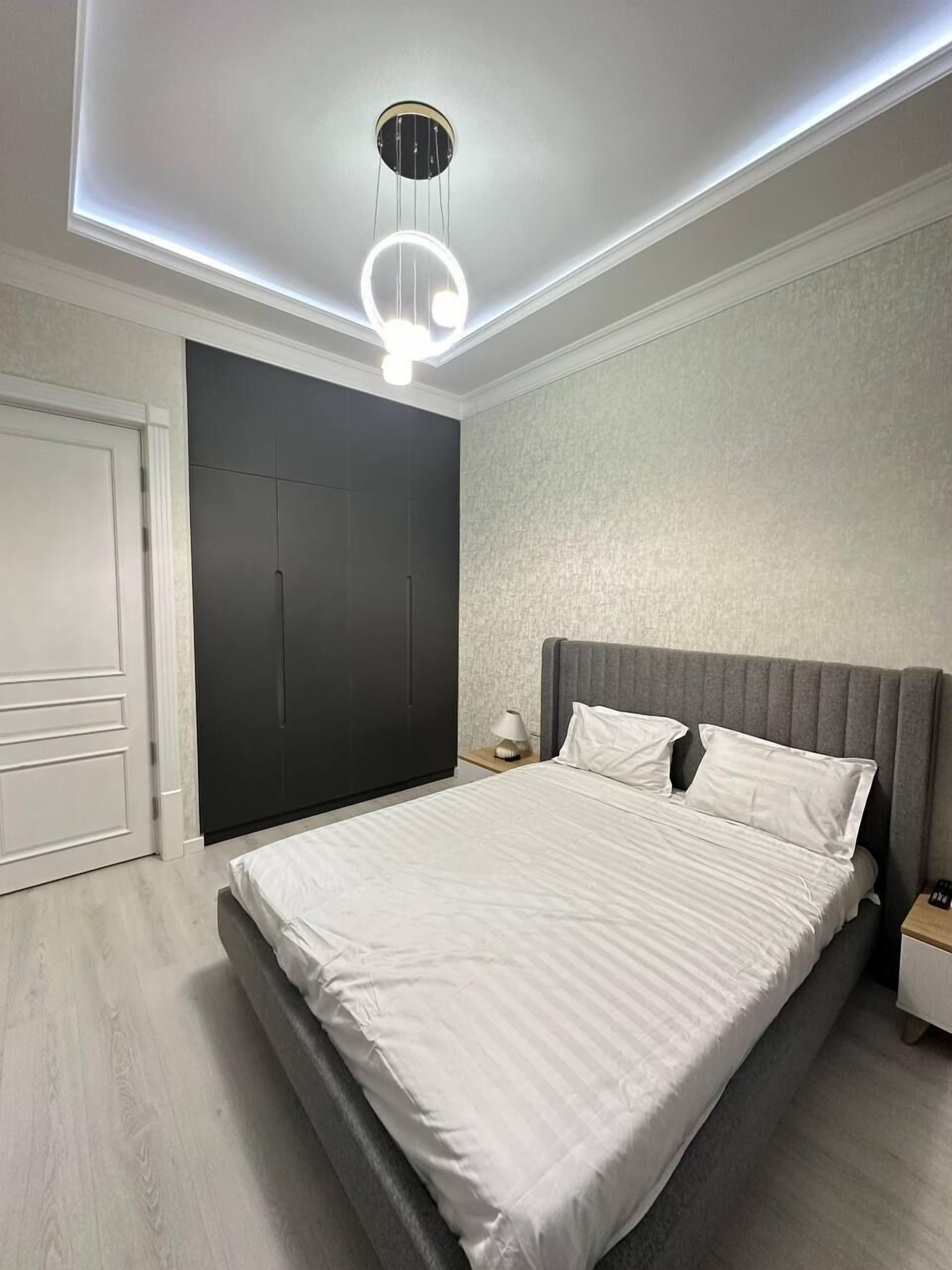 A modern bedroom with a bed, a nightstand, a wardrobe, and a ceiling light fixture.