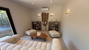 A modern living room with a large tufted sofa, a wooden coffee table, and two matching ottomans. There are decorative wall sconces and a wooden accent wall piece. - Villa with swimming pool on the Angoulême golf course (Angoulême)