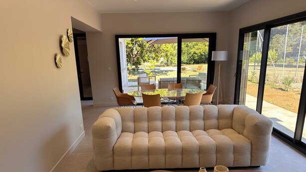 A modern living room with a beige sectional sofa, a wooden coffee table, and a glass door leading to an outdoor patio with a dining set. - Villa with swimming pool on the Angoulême golf course (Angoulême)