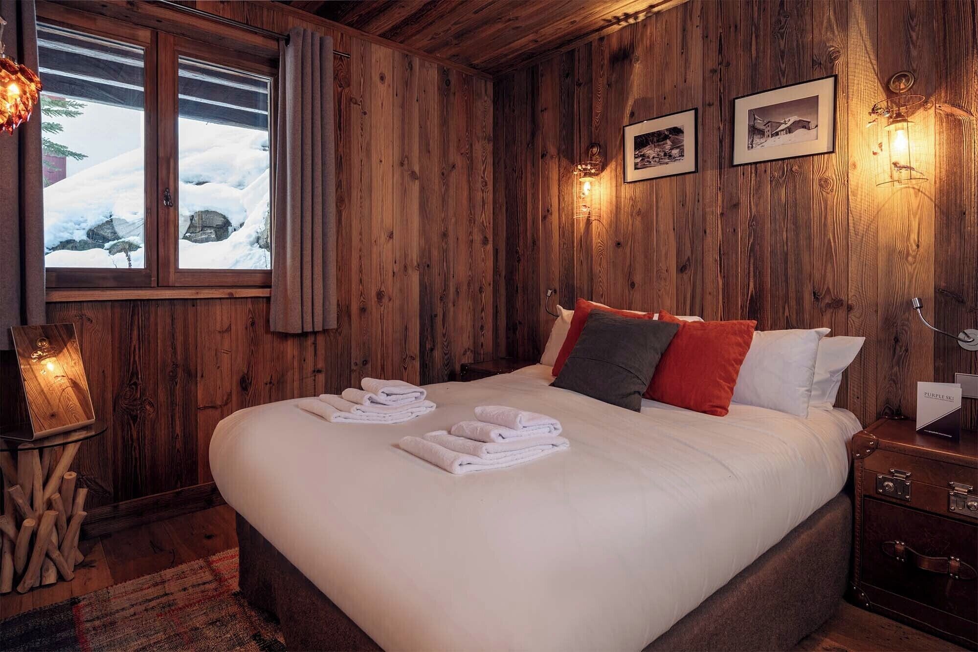 Une chambre aux murs lambrissés, avec un lit, des serviettes et des tableaux encadrés.