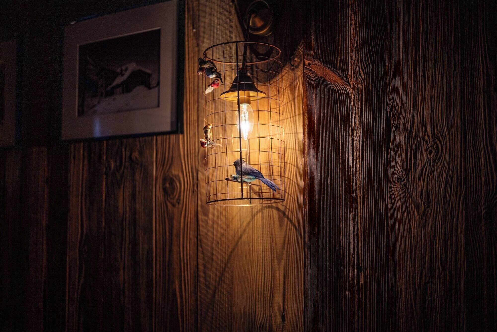 Une cage à oiseaux avec une ampoule à l’intérieur, fixée à un mur en bois.
