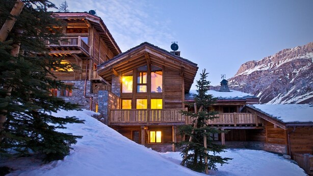A wooden lodge with multiple balconies and large windows, surrounded by snow and trees.