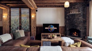 A cozy living room with a stone fireplace, leather sofas, and a television displaying 'UNIVERSAL'.