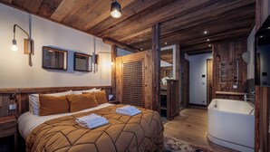 A bedroom with a large bed, wooden ceiling, and a bathroom with a bathtub.