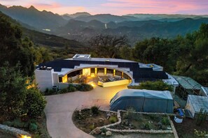 Uma casa moderna com telhado curvo, um pátio com assentos e vista para montanhas ao redor.