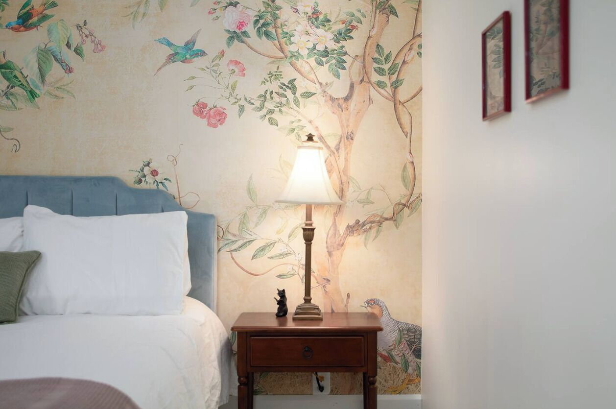Um quarto com uma cama, uma mesa de cabeceira com abajur e uma parede com um mural floral.