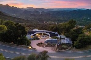 A modern house with a curved roof, surrounded by lush greenery and mountains in the background.