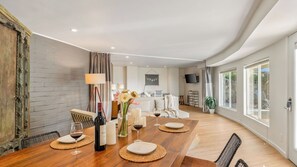 Uma sala de jantar com mesa de madeira posta para quatro pessoas, uma garrafa de vinho e velas.
