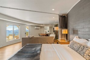 Quarto de hotel moderno com cama grande, sofá, área de refeições e vista para montanhas.