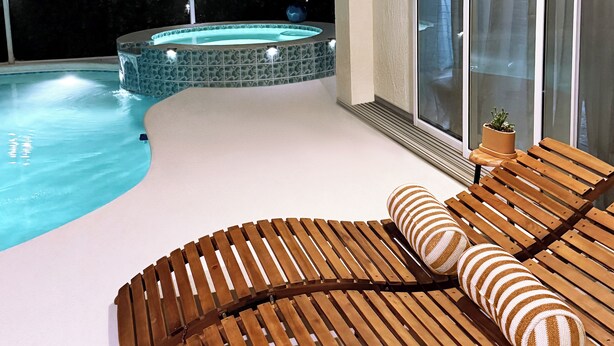 Ett område vid poolen med en bubbelpool och solstolar i trä.