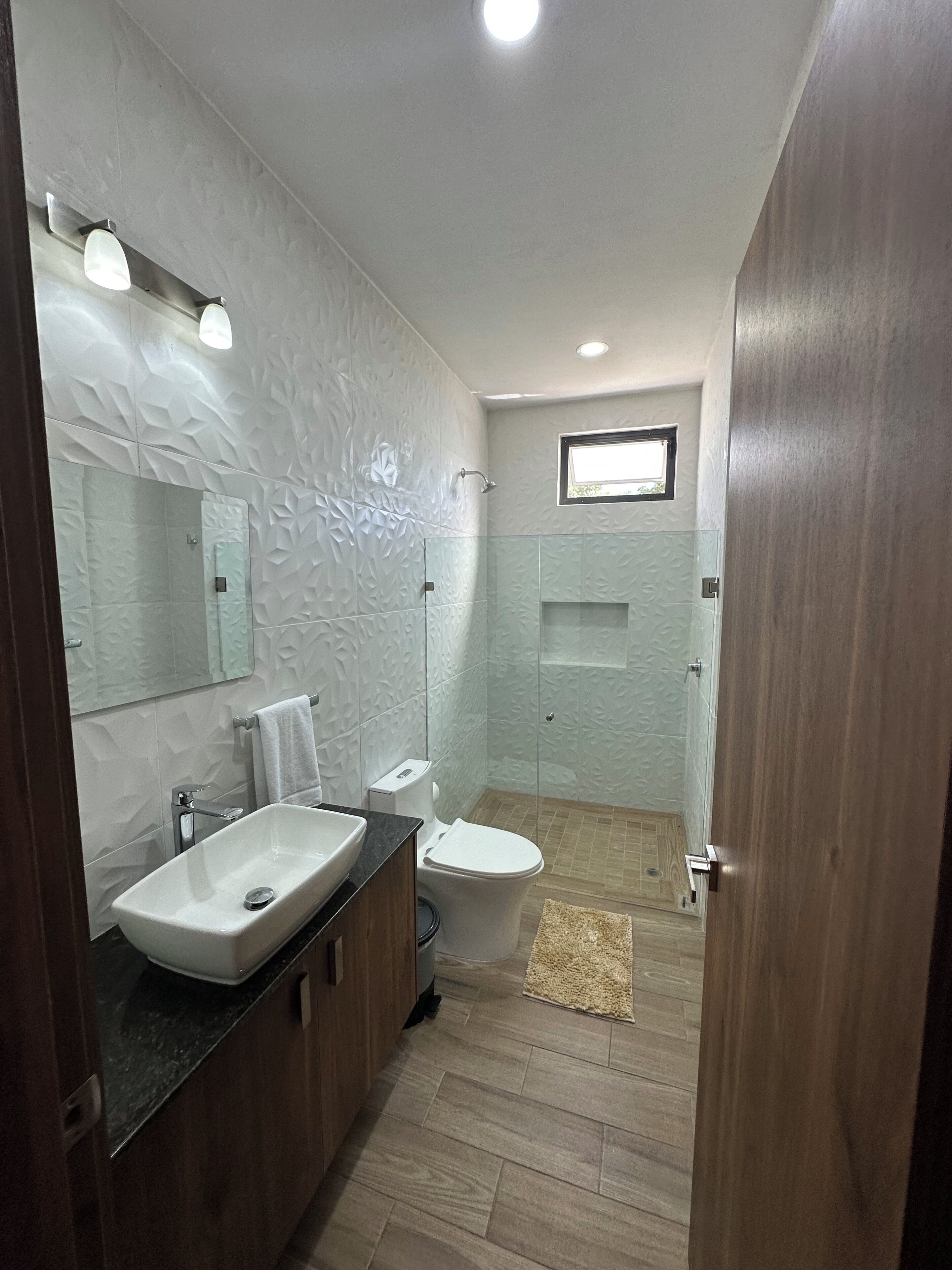 A modern bathroom with a large mirror, a sink, a toilet, and a shower area.