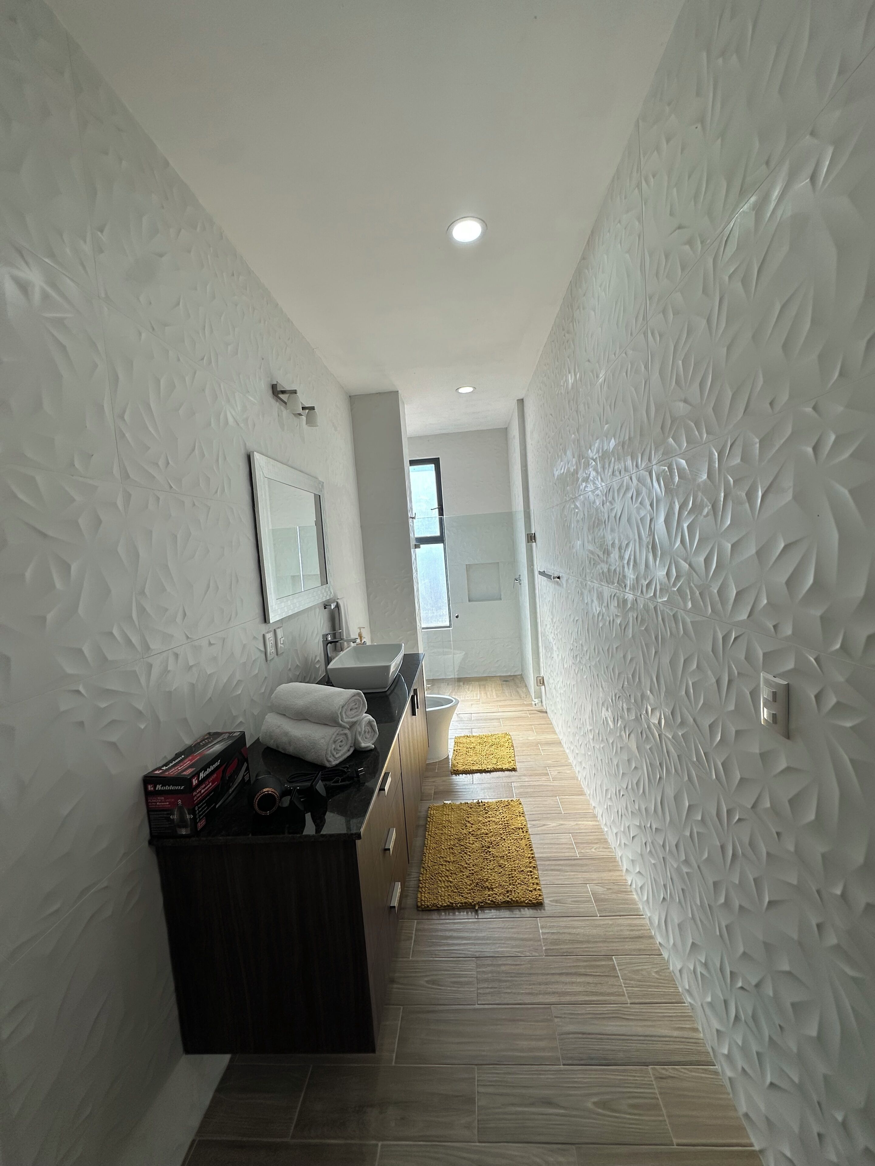 Un baño moderno con tocador, espejo, lavabo y perchero para toallas.