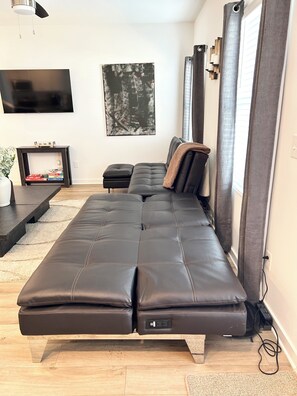 A modern living room with a sofa, a flat-screen TV, a painting, and a window with curtains.