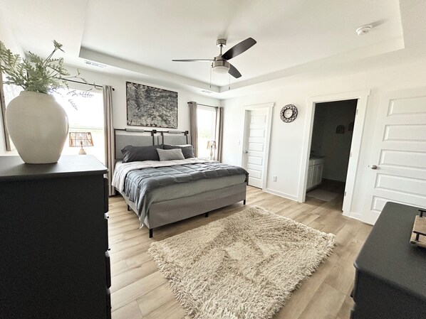 Een slaapkamer met een bed, een plafondventilator, een vloerkleed en een deur naar een andere kamer.