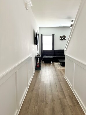 A modern interior with a wooden floor, a black sofa, a flat-screen TV, and a ceiling fan.