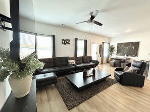 A modern living room with a sectional sofa, a coffee table, a floor lamp, and a ceiling fan. - Spacious Stay with 2-Car Garage & Multiple TVs (Huntsville)