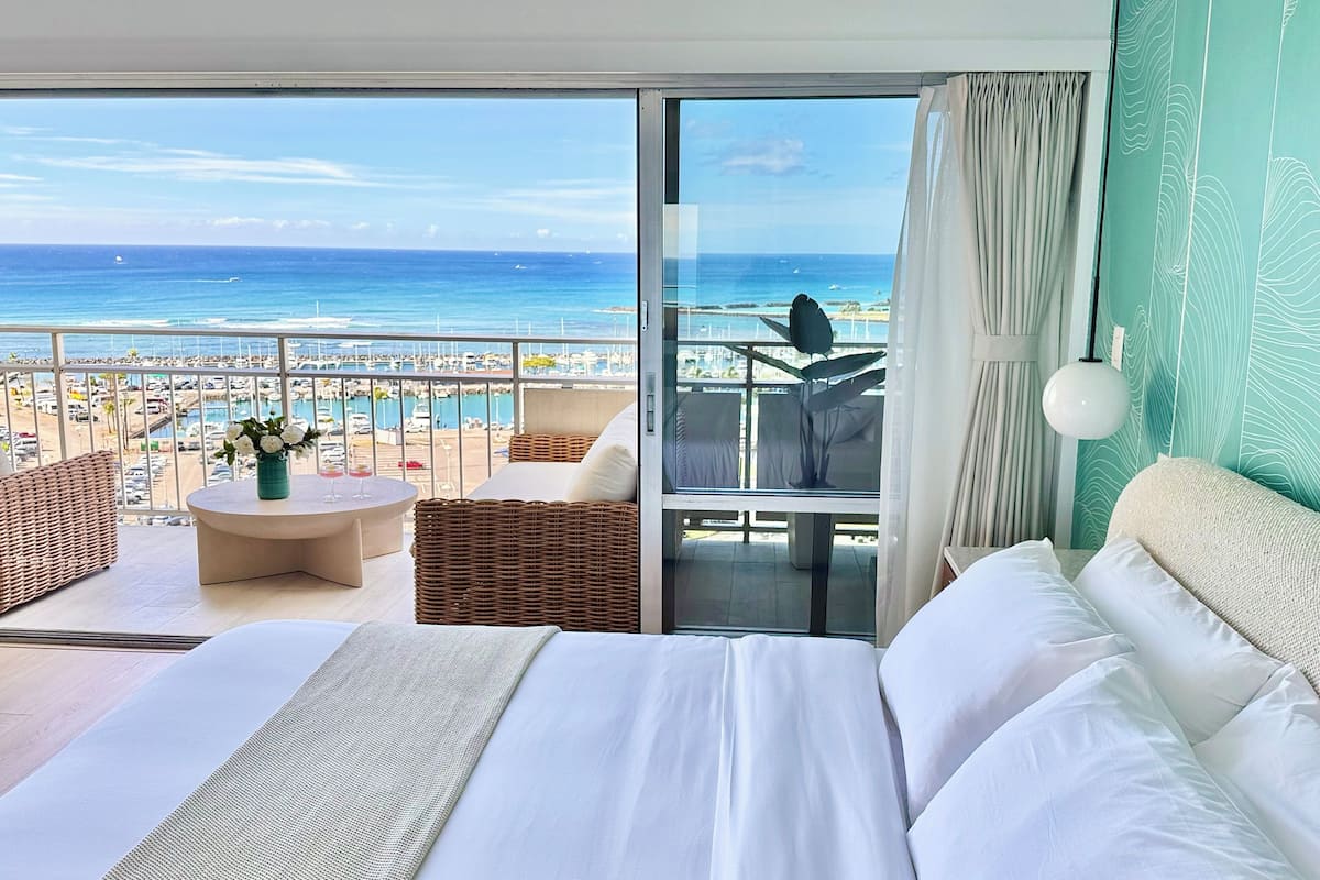 A hotel room with a balcony overlooking a marina and the ocean.