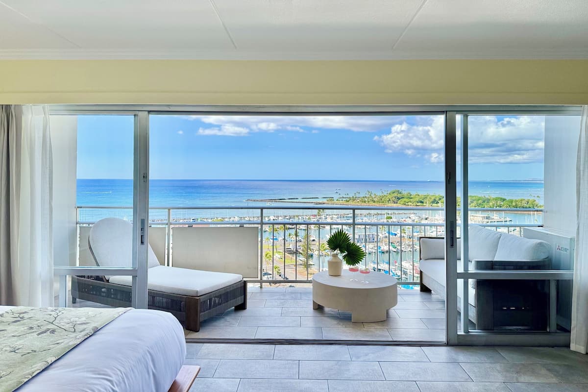 A hotel room with a balcony overlooking a marina and the ocean.
