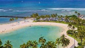 A beach with clear turquoise waters, palm trees, and a parking area with cars. - Panoramic Oceanview Resort (Honolulu)