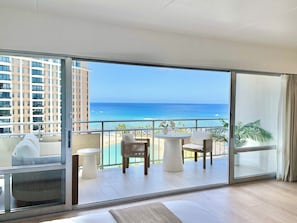 Un balcon avec vue sur l’océan, un coin salon avec une table et une grande fenêtre.