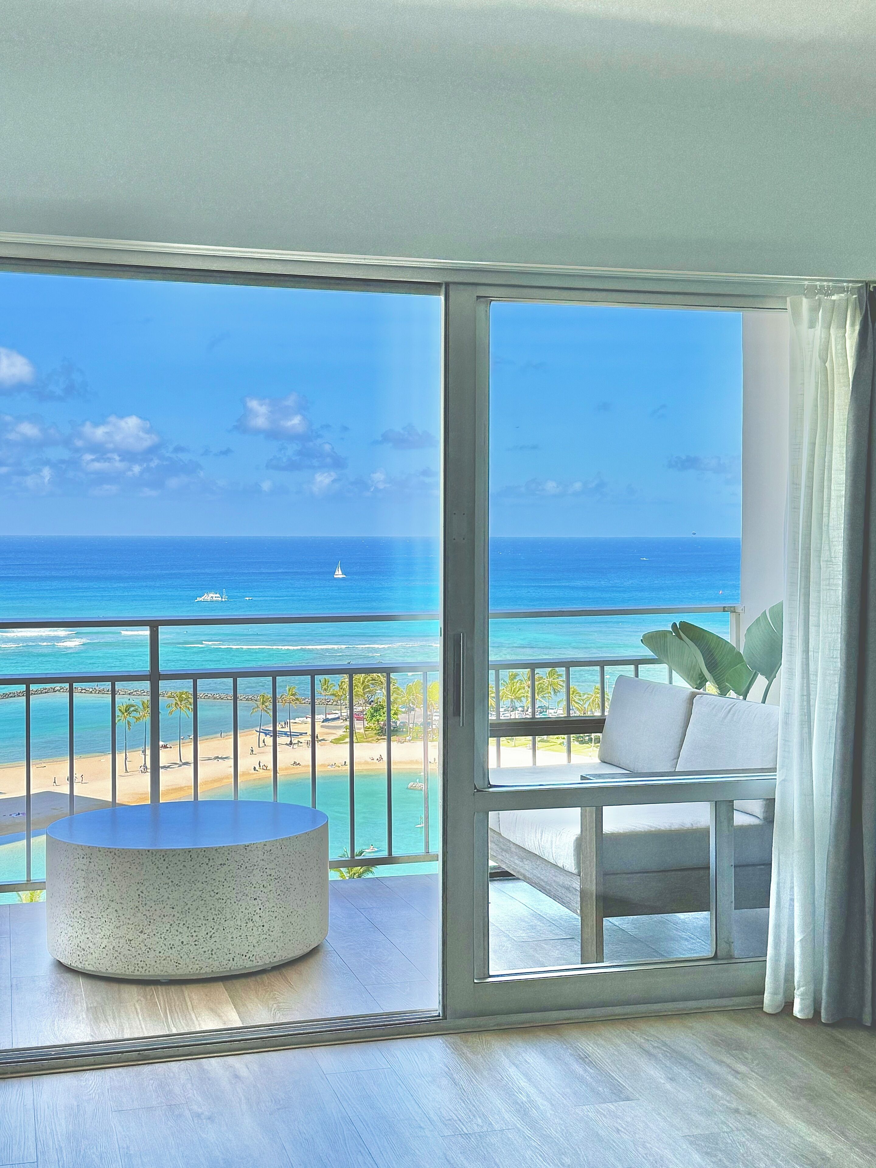 A balcony with a view of the ocean, a round table, and a sofa with cushions.