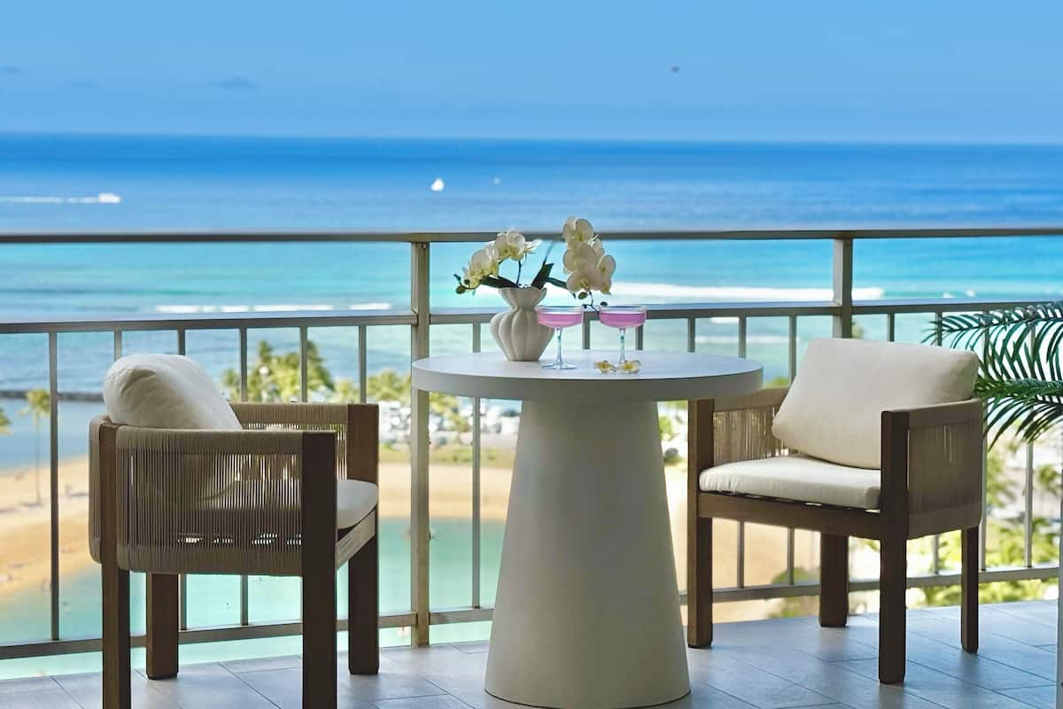 A balcony with a view of the ocean, a round table with two chairs, and a vase with flowers.