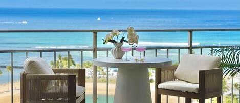 A balcony with a view of the ocean, a round table with two chairs, and a vase with flowers.