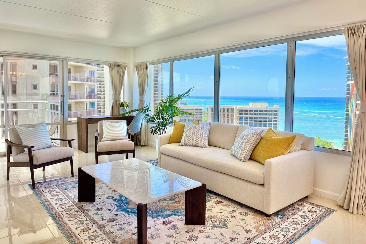 A modern living room with a large window offering a view of the ocean and high-rise buildings.