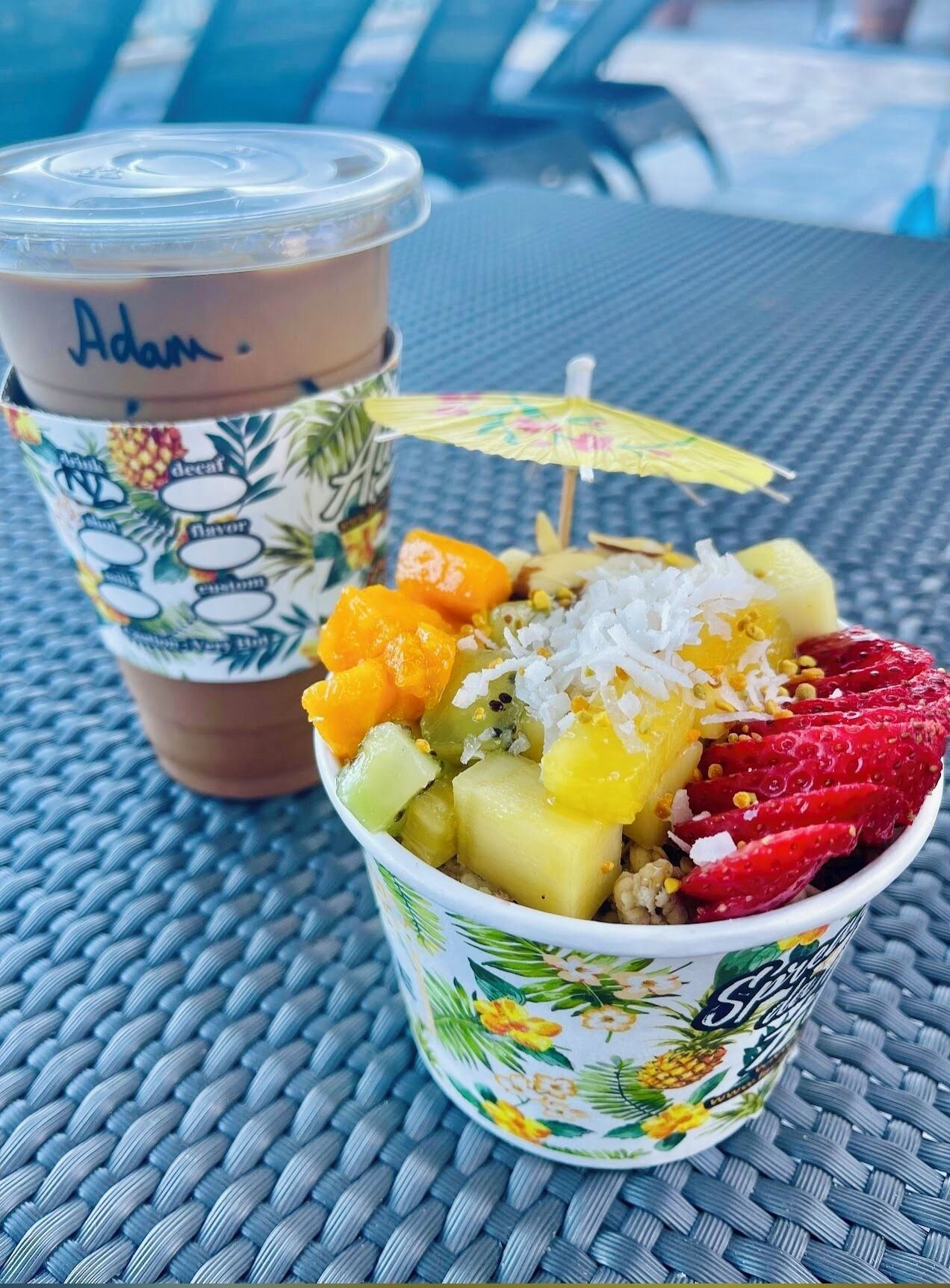 A cup of iced coffee with a straw and a paper cup with a tropical design.