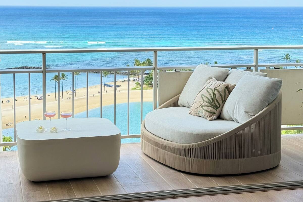 A balcony with a view of the ocean, a round sofa, and a small table with drinks.