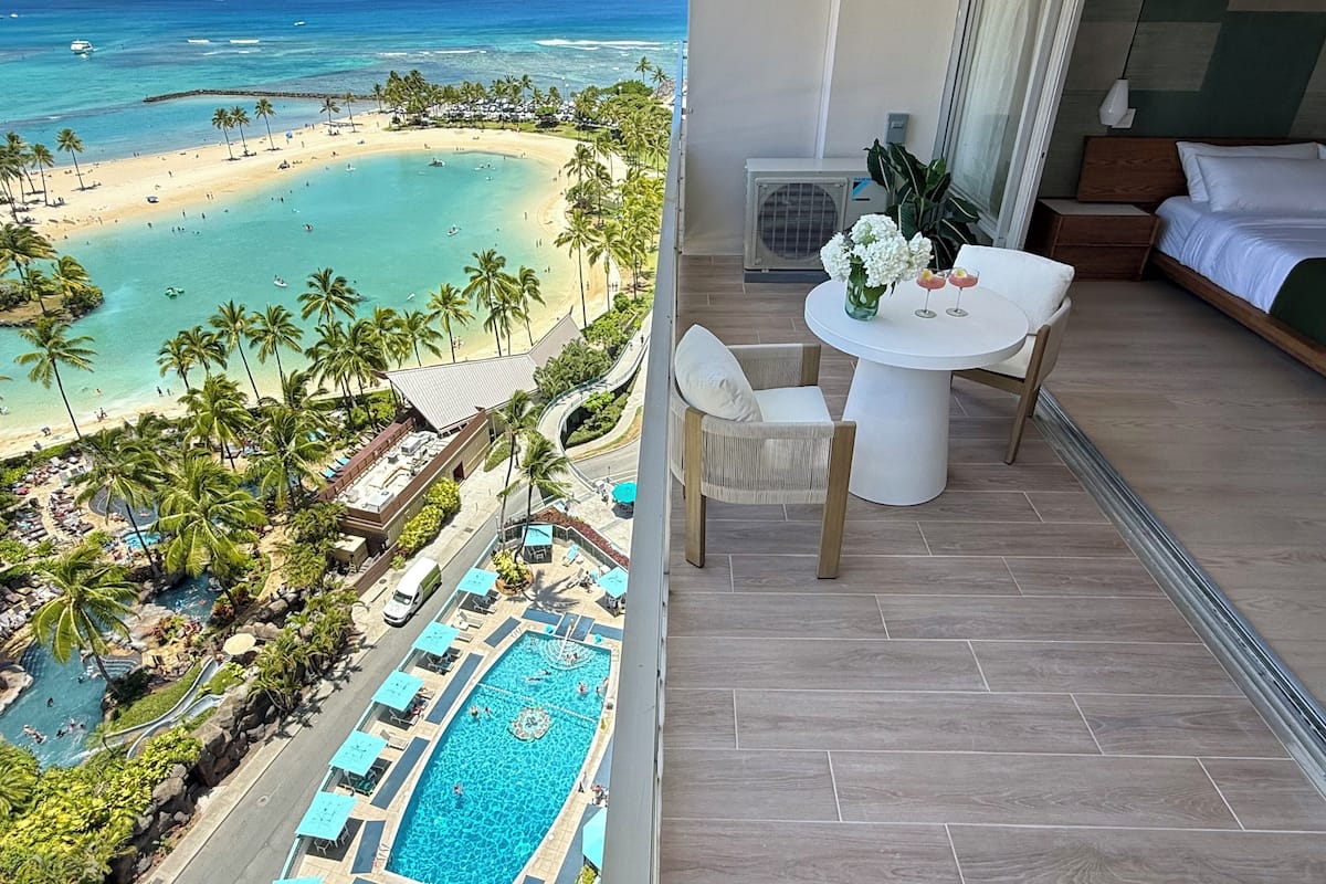 A balcony with a pool, a beach view, and a dining area with a table and chairs.