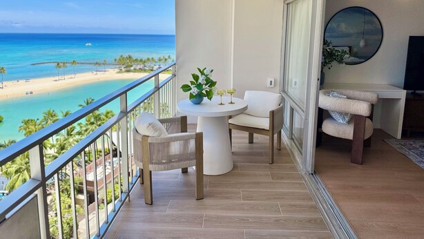 A balcony with a view of a beach and ocean, furnished with a table, chairs, and a cat tree. - Panoramic Oceanview Resort (Honolulu)