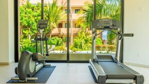 Ein Fitnessraum mit zwei Laufbändern und einem Crosstrainer, große Fenster mit Blick auf Grünflächen und Gebäude.